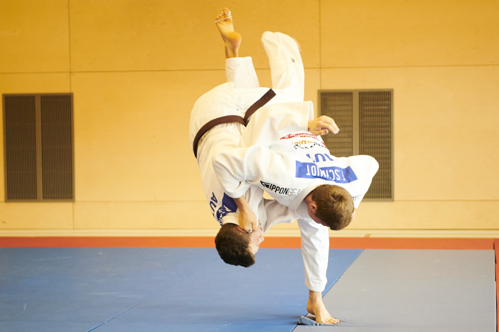 Kind im weißen Judoanzug wird bei einem Wurf kopfüber durch die Luft geworfen