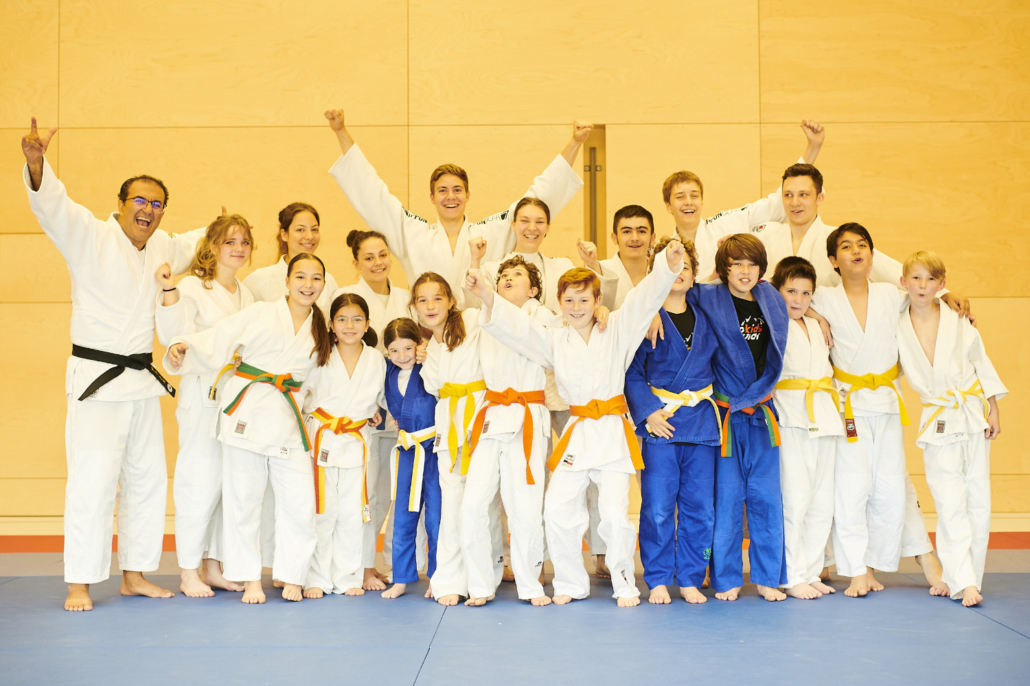 Gruppenfoto der Judokids mit bunten Gürteln, viele jubeln in die Kamera